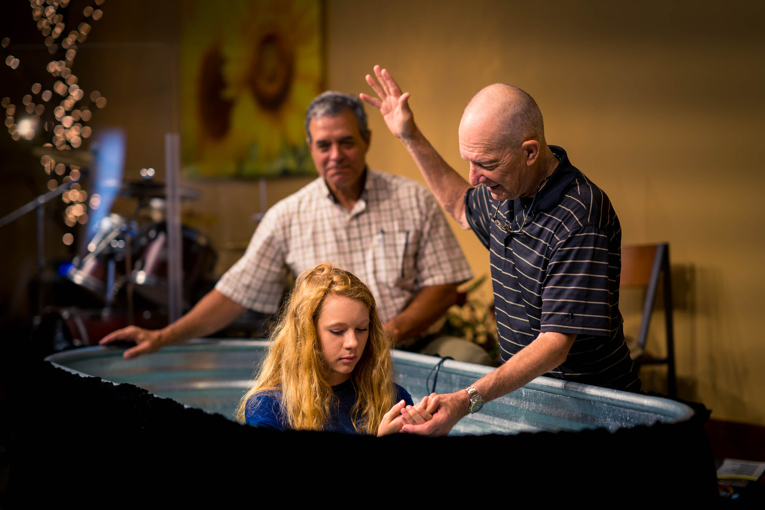 girl in baptism tub indoor church with two elders baptizing